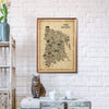 The Bronx Antique illustrated map poster in a warm wood frame hanging on a white brick wall above a small table, with a tabby cat, vintage furniture, flowers, and neutral home decor.