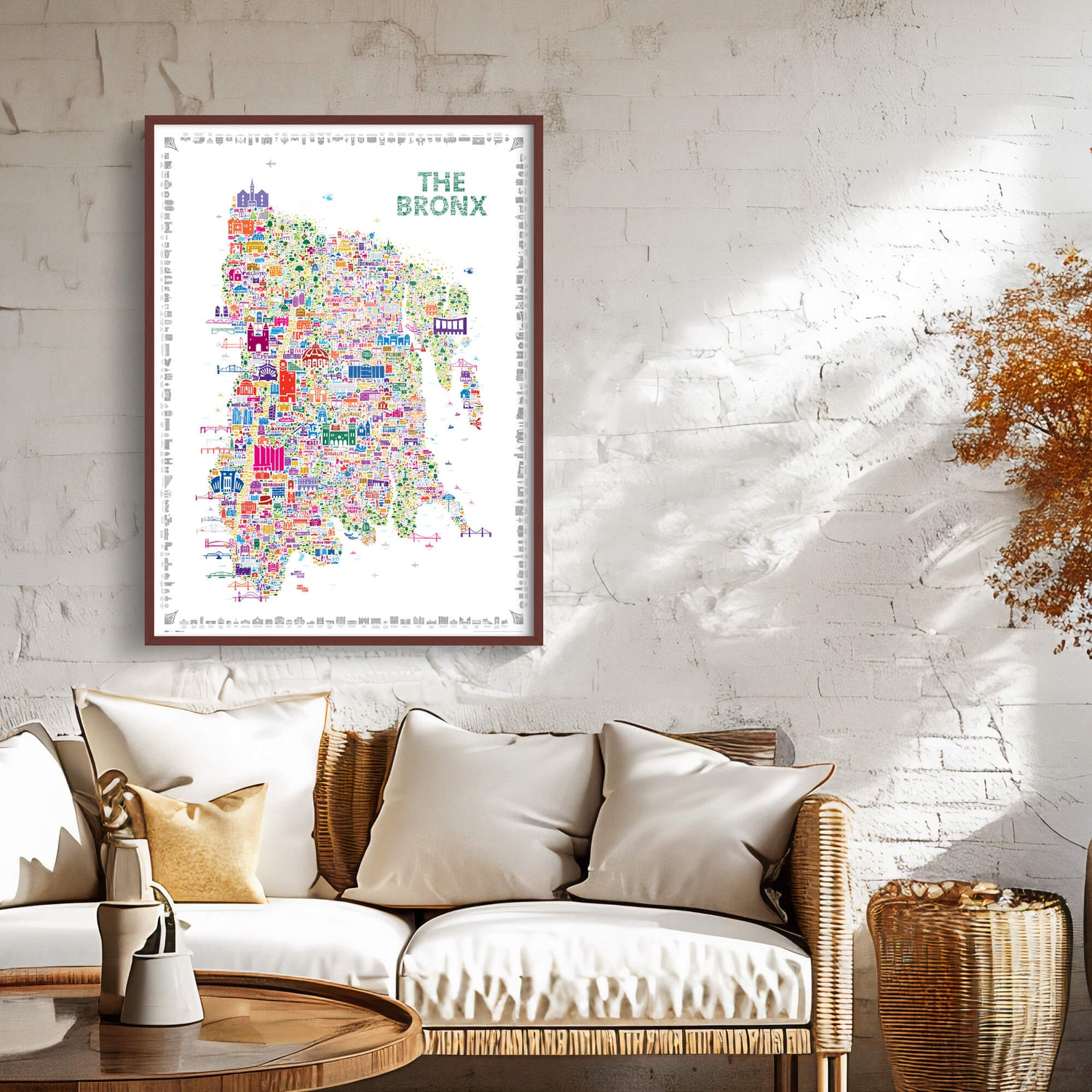 Colorful The Bronx illustrated map poster framed above a cream sofa in a bright living room with textured white walls, woven furniture, neutral cushions, and warm natural accents.