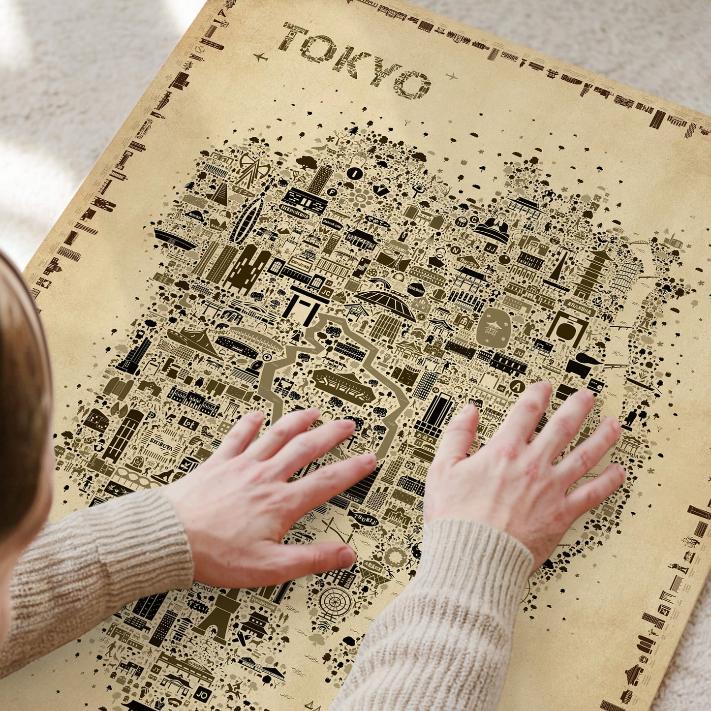 Close-up of hands touching a Tokyo Antique illustrated map poster, showing detailed landmarks and icons in a vintage sepia design.