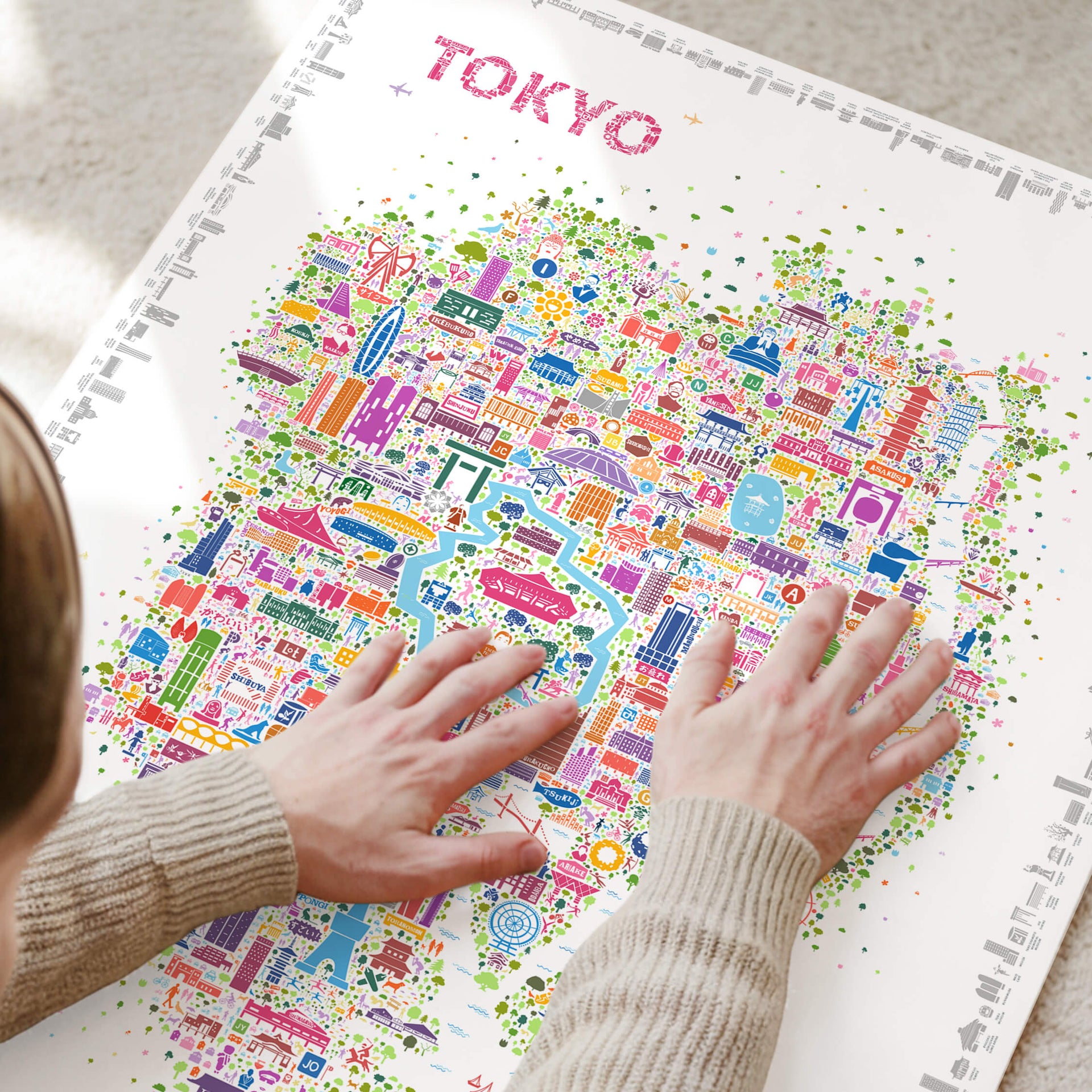 Close-up of hands touching a colorful Tokyo illustrated map poster, showing detailed landmarks and icons in vibrant colors.
